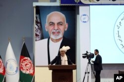 FILE - Backdropped by his own image, Afghan President Ashraf Ghani speaks to delegates during the first day of the Afghan Loya Jirga meeting in Kabul, Afghanistan, April 29, 2019.