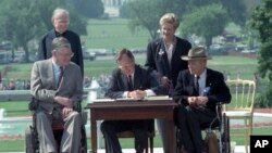 President George Bush signs the Americans with Disabilities Act during a ceremony on the South Lawn of the White House July 26, 1990. 