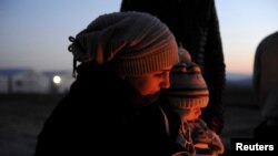 FILE - A Syrian refugee holds her baby next to a bonfire as she waits to cross the Greek-Macedonian border, near the village of Idomeni, Greece, Jan. 21, 2016.