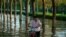 FILE - A man pushes a scooter through floodwaters in Xinxiang in central China's Henan Province, July 26, 2021. 