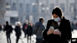 A woman wearing a sanitary mask looks at her phone in Milan, Italy, Monday, Feb. 24, 2020. 