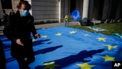 FILE - A man with a face mask and a child with an European flag attend an event of the Pulse of Europe movement to collect signatures for more support for Italy during the COVID-19 outbreak in front of the Italian embassy in Berlin, April 22, 2020.