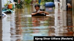 Seorang pria membawa barang-barangnya mengarungi genangan air yang merendam jalan menyusul hujan lebat di Jakarta, Sabtu, 20 Februari 2021. (Foto: Ajeng Dinar Ulfiana/Reuters)