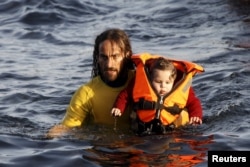 A volunteer lifeguard holds a baby as a half-sunken catamaran carrying around 150 refugees, most of them Syrians, arrives after crossing part of the Aegean sea from Turkey on the Greek island of Lesbos, Oct. 30, 2015.