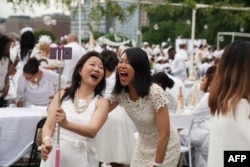 FILE - Women laugh as they attend "Diner en Blanc" at the Nelson Rockefeller Park in Battery City in New York on July 17, 2019. (Photo by TIMOTHY A. CLARY / AFP)