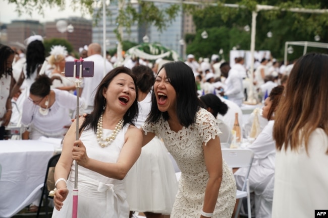 FILE - Women laugh as they attend "Diner en Blanc" at the Nelson Rockefeller Park in Battery City in New York on July 17, 2019. (Photo by TIMOTHY A. CLARY / AFP)