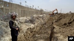 FILE - A Pakistani border guard stands on alert as an excavator digs a trench along the Pakistan-Afghanistan border at Chaman post in Pakistan, May, 16, 2014.