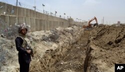 FILE - A Pakistani border guard stands alert as an excavator digs a trench along the Pakistan-Afghanistan border at Chaman post, in Pakistan, May 16, 2014.