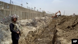 FILE - A Pakistani border guard stands guard as an excavator digs a trench along the Pakistan-Afghanistan border at Chaman post in Pakistan, May, 16, 2014.