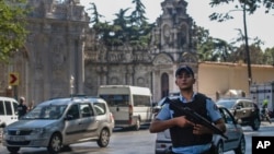A Turkish police officer secures the road that leads to Istanbul's Dolmabahce Palace, background, Aug. 19, 2015, following an armed attack.
