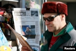 FILE - A man walks past a rack which displays a daily newspaper with a front page about Russian President Vladimir Putin’s re-election victory on March 18, on a street in Moscow, Russia, March 19, 2018.