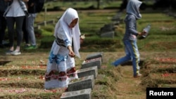 A girl places flowers on the graves of some of the victims who died during the political turmoil of 1998 during a 20th anniversary commemoration at Pondok Ranggon mass grave in Jakarta, Indonesia, May 13, 2018. 