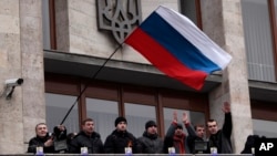 FILE - In this March 5, 2014 file photo, pro-Russia demonstrators holding a Russian flag, with the Ukrainian emblem in the background, stand on the balcony of the regional administrative building after storming it in Donetsk, Ukraine