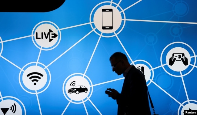 FILE - A man looks at his phone in front of a stand at the Mobile World Congress in Barcelona, Spain, Feb. 28, 2017.