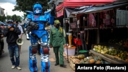 Seorang mengenakan kostum Transformers dan petugas lainnya mengingatkan warga agar tetap tinggal di rumah selama PSBB di Bandung, Jawa Barat (Foto: Antara/Reuters). 