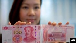 FILE - A staff member displays the new version of the 100-yuan RMB banknotes (US 15.7 dollars) to photographers at the Bank of China Tower in Hong Kong, Nov. 12, 2015.