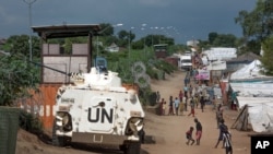 FILE - Civilians sheltering in a U.N. base in South Sudan's capital, Juba, for fear of targeted killings by government forces walk by an armored vehicle and a watchtower, July 25, 2016.