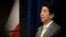 Japan's Prime Minister Shinzo Abe speaks next to the Japanese national flag, attached with a black ribbon to mourn victims a day before the third anniversary of the March 11, 2011 earthquake, tsunami and nuclear crisis.