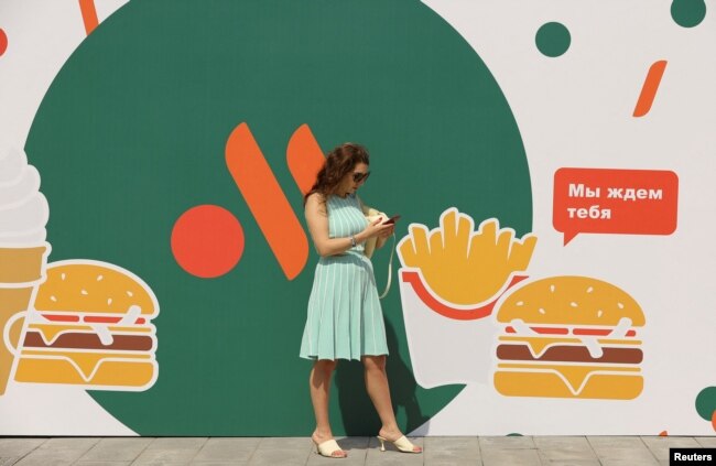 Seorang perempuan berdiri di samping logo restoran "Vkusno & tochka" yang mengambil alih bisnis McDonald's setelah waralaba AS ini hengkang dari Rusia (foto: dok.)