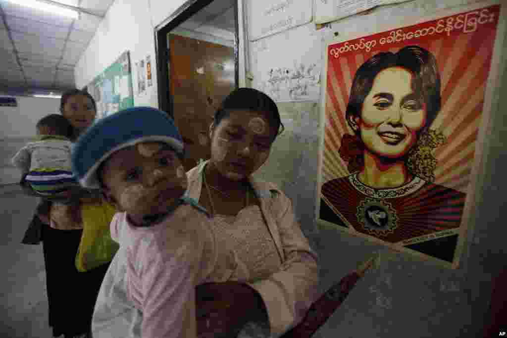 Migrant workers from Burma hold their children as they stand near a portrait of Burma's pro-democracy leader Aung San Suu Kyi at the Mae Tao clinic in the Thai border town of Mae Sot, November 10, 2010.