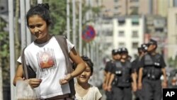 ***File*** A woman and a child walk ahead of police officers patrolling on a street in Urumqi in northwest China's Xinjiang Uygur Autonomous Region Friday, July 2, 2010. Chinese authorities have stepped up security measures ahead of the anniversary of a d