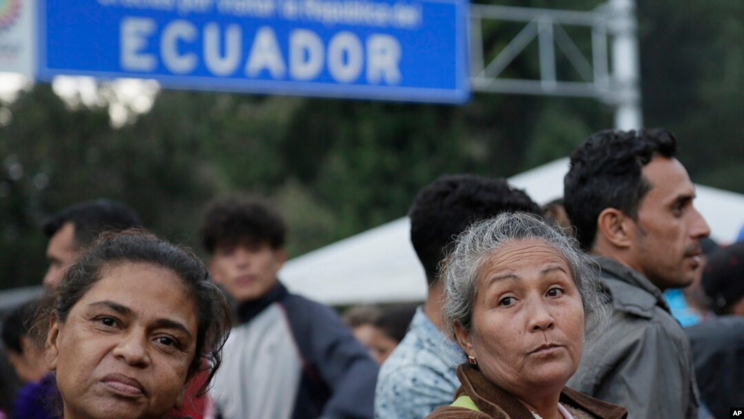 ARCHIVO - Migrantes esperan afuera de una oficina de procesamiento de inmigración en el puente de Rumichaca después de cruzar la frontera de Colombia a Rumichaca, Ecuador, el miércoles 12 de junio de 2019.