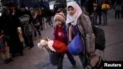 A Syrian girl carries her dolls as refugees and migrants arrive aboard a passenger ferry at the port of Piraeus, near Athens, Greece, Jan. 13, 2016. 