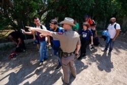 FILE - A Texas Department of Public Safety officer directs a group of migrants who crossed the border and turned themselves in, in Del Rio, Texas, June 16, 2021.