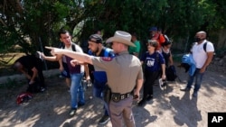 FILE - A Texas Department of Public Safety officer directs migrants who crossed the border and turned themselves in, in Del Rio, Texas, June 16, 2021.