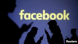 FILE - Silhouettes of mobile users are seen next to a screen projection of Facebook logo in this picture illustration taken March 28, 2018.