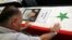 A Syrian man mourns a relative whose picture is displayed atop his coffin with Arabic words that read: "The Martyr, Atef Abdullah" during a mass funeral procession for several Syrians killed in a twin suicide bombings, at a mosque in Damascus, Syria Satur