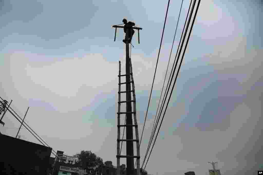 An Indian electricity department worker climbs on a pole to fix power lines as monsoon clouds gather above in Jammu.