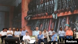 Colombia's President Juan Manuel Santos, front left, top commander of the Revolutionary Armed Forces of Colombia, FARC, Rodrigo Londono, also known as Timoleón Jiménez or Timochenko, front right, and Jean Arnault, U.N. representative for the Colombian peace process, center, watch the disarmament process on a television monitor during an act to commemorate the completion of the disarmament process, in Buenavista, Colombia, June, 27, 2017. 