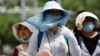 Warga Beijing mengenakan perlengkapan pelindung matahari saat berjalan di jalanan kota pada 1 Juli 2023, di tengah gelombang panas. (Foto: REUTERS/Tingshu Wang)