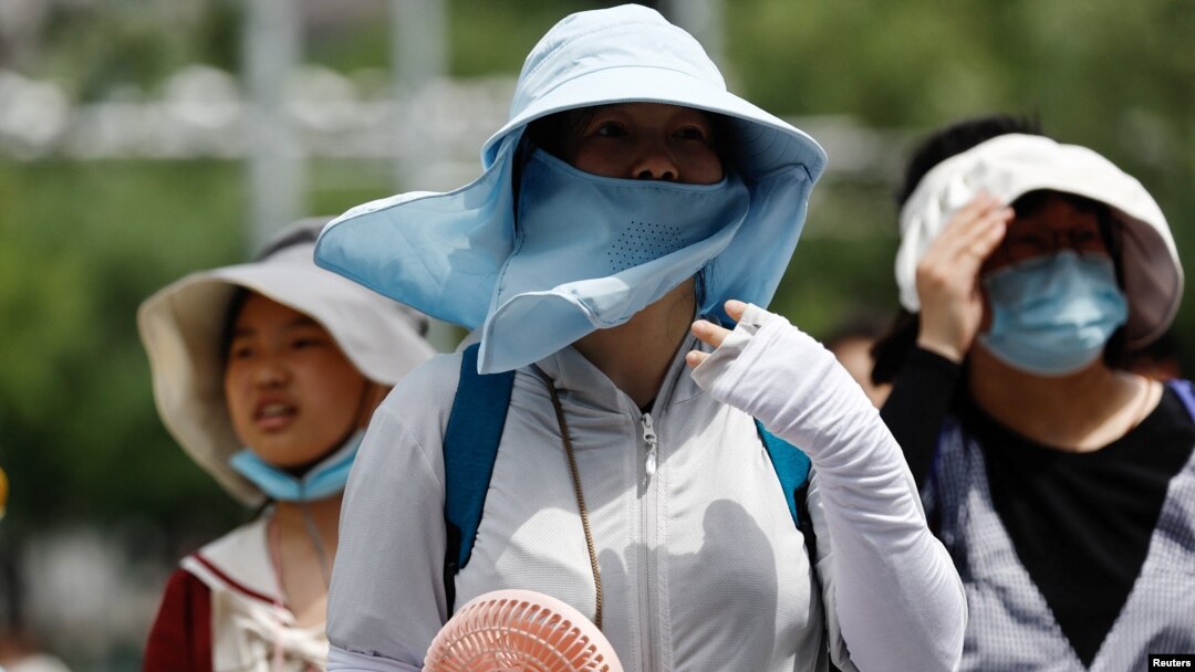 Warga Beijing mengenakan perlengkapan pelindung matahari saat berjalan di jalanan kota pada 1 Juli 2023, di tengah gelombang panas. (Foto: REUTERS/Tingshu Wang)