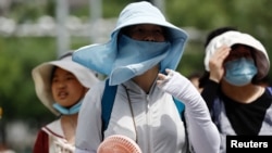 Warga Beijing mengenakan perlengkapan pelindung matahari saat berjalan di jalanan kota pada 1 Juli 2023, di tengah gelombang panas. (Foto: REUTERS/Tingshu Wang)