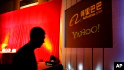 In this file photos, a man walks past a screen displaying the Yahoo and Alibaba.com logos before a joint news conference by the companies at the China World Hotel in Beijing, Aug. 11, 2005. (AP Photo/Elizabeth Dalziel, File)