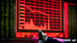 An investor rests her leg on a bench near an electronic board displaying stock prices at a brokerage house in Beijing, Jan. 4, 2016.