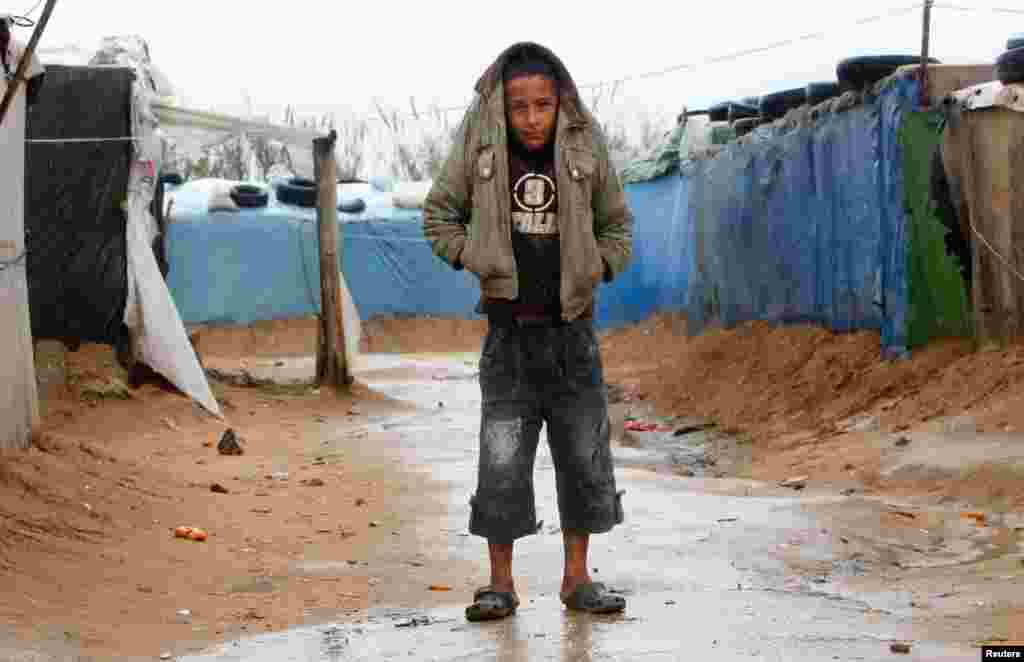 Seorang bocah lelaki memakai jaketnya sebagai payung di tengah hujan yang turun di sebuah kamp pengungsi di Tyre, Lebanon selatan. 