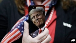 A woman holds up her phone before a rally with Republican presidential candidate Donald Trump in Bedford, New Hampshire, Sept. 29, 2016. In an interview to air Sunday, Trump has signalled that as president he will exercise more restraint on Twitter.