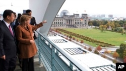 La chancelière allemande Angela Merkel, à droite, debout à côté du vice-président de la Chine, Xi Jinping, à gauche, à la chancellerie de Berlin, en Allemagne, le 12 octobre 2009. Elle pointe son doigt vers le bâtiment du parlement allemand Reichstag 