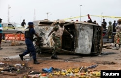 A soldier and a paramilitary officer help to move part of a damaged car at the scene of a car bomb attack in Nyanya, Abuja, May 2, 2014.