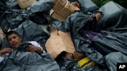 FILE - Central American migrants use trash bags and cardboard to protect themselves from the rain as they wait atop a stuck freight train, outside Reforma de Pineda, Chiapas state, Mexico, June 20, 2014.