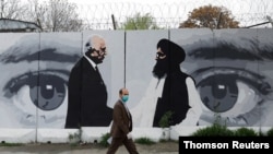 FILE - An Afghan man wearing a protective face mask walks past a wall painted with photos of Zalmay Khalilzad, U.S. envoy for peace in Afghanistan, and Mullah Abdul Ghani Baradar, the leader of the Taliban delegation, in Kabul, Afghanistan.