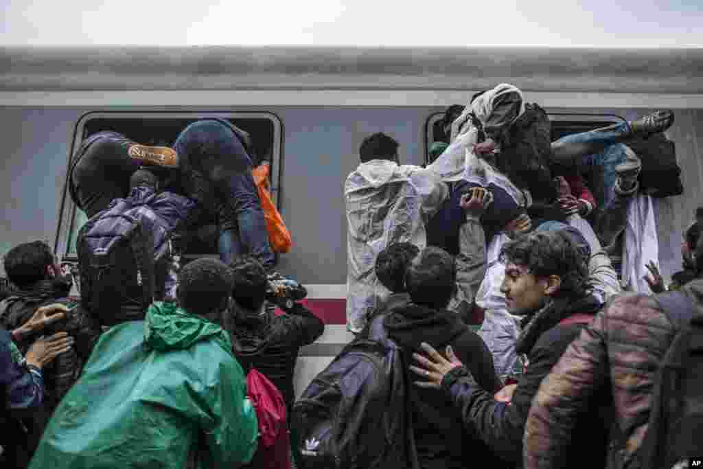 Migrants and refugees board a train by climbing through the windows as they try to avoid a police barrier at the station in Tovarnik.