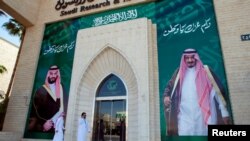 FILE - Men walk past murals depicting Saudi Arabia's King Salman bin Abdulaziz Al Saud and Crown Prince Mohammed bin Salman, in Riyadh, Saudi Arabia, Nov. 9, 2017.