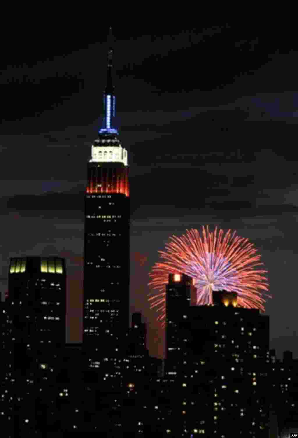 The Empire State Building, illuminated with red, white and blue lights is seen from across the East River in the Queens borough of New York, backlit by fireworks exploding over the Hudson River during the Macy's Fourth of July fireworks show on Monday, Ju