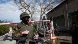 Ukrainian servicemen look on as an armed man, believed to be a Russian soldier, stands guard inside a Ukrainian military base in the Crimean town of Yevpatoria, March 5, 2014.