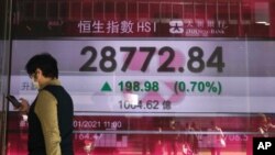 A woman walks past a bank's electronic board showing the Hong Kong share index at Hong Kong Stock Exchange, Jan. 18, 2021. 