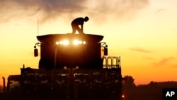 FILE - A corn farmer, on top of his combine, is silhouetted against the setting sun while harvesting corn in Pleasant Plains, Illinois, Sept. 27, 2014. 
